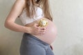 A girl pregnant at the ninth month holds a knitted rattle in the form of a lion in her hands on a monochrome light background. An