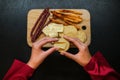 Girl prepares snacks top view. female hand takes bread with cheese from a common plate of snacks. sausage, camembert, suluguni on Royalty Free Stock Photo