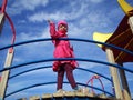 A girl of preschool age climbed to the top of the structure in the playground and waves her hand. The child has glasses. Pink Royalty Free Stock Photo