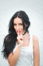 Girl presses index finger to her lips. Portrait of a beautiful young woman in a white t-shirt with black hair presses her index