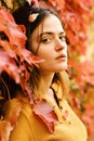 Girl with pretty hair enjoys fall time. Lady posing near red leaves. Woman with passionate face