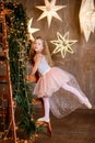 girl in a princess dress of a ballerina stands on a stepladder decorated with green spruce branches