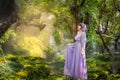 Girl in a princess dress is in a mysterious deep forest with trees, flowers and waterfalls