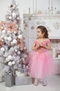 Girl in a princess dress stands near a Christmas tree and makes a wish