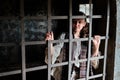 A girl prisoner with a sad smile looks through the bars in a dark prison