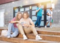 Girl prompts solution to problem to young man sitting on stone staircase in front of school