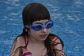 Girl with protective goggles and red swimsuit splashing in swimming pool. Adorable little girl in outdoor swimming pool Royalty Free Stock Photo