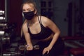 The girl in a protective mask is engaged in dumbbells. Protective masks against virus infection. Training during quarantine in the