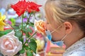 A girl in a protective mask holds a bouquet of flowers and sniffs roses, quarantined for the duration of the covid-19 virus