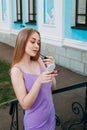 Girl in a purple dress paints her lips with lipstick, near the blue facade of a beautiful old building Royalty Free Stock Photo