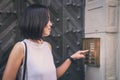 Girl that is pushing a button of the house intercom outdoors in front of a huge antique door.