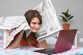 Girl put newspapers to her head and looks at the laptop screen trying to find work