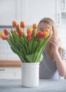 The girl puts a beautiful bouquet of red and yellow tulips in a white vase on a wooden countertop against the background of a Royalty Free Stock Photo