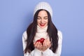 Girl puts her hands together and Christmas tree bauble lies on them, brunette female wearing warm white clothing looking at her Royalty Free Stock Photo