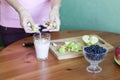 The girl puts the pieces of green apples in a glass of yogurt