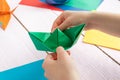 A girl puts together an origami crane and a boat made of colored paper. On a wooden background Royalty Free Stock Photo
