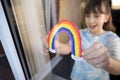Girl Putting Picture Of Rainbow In Window At Home During Coronavirus Pandemic To Entertain Children Royalty Free Stock Photo