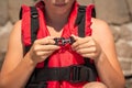 Girl putting on red life jacket on beach. Female hands fastens plastic buckle clasp of life vest. Safety during water sports Royalty Free Stock Photo