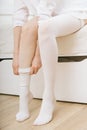 Girl putting on white stockings at home. Anti-embolic stockings. Compression Hosiery. Medical stockings, tights, socks Royalty Free Stock Photo