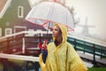 Girl in rain suit with umbrella stay on bridge with dutch mills