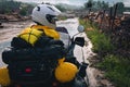 A girl in a raincoat, shoe covers and a helmet is sitting on big adventure motorbike. Rain and felling after the storm. Sawmill.