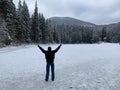 A girl with raised hands looks at the winter forest in the mountains. A woman stands on a frozen lake. A person admires the beauty