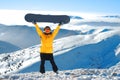 Girl raises snowboard up against panoramic winter mountain