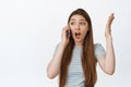Girl reacts to phone call with surprised, excited emotion, raising hands up and gasping in awe, talking on mobile