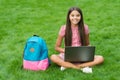 Girl reacts while using a laptop sit on green grass in park with school back, education