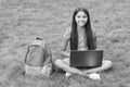 girl reacts while using a laptop sit on green grass in park with school back, education