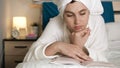 Girl is reading book. Attractive woman in bedroom in white bathrobe with towel on her head lies on stomach and reads book, turns Royalty Free Stock Photo