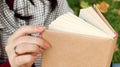 Girl reading a book in the autumn park. Female hands open the pages of a paper book outdoors on a warm sunny day. The student is Royalty Free Stock Photo