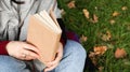 Girl reading a book in the autumn park. Female hands open the pages of a paper book outdoors on a warm sunny day. The student is Royalty Free Stock Photo