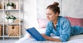 Girl reading book in bed, lying on her stomach, smiling happy and relaxed Royalty Free Stock Photo