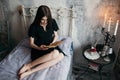 A girl is reading a book on a bed in a romantic black dress. Royalty Free Stock Photo