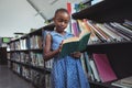 Girl reading book by bookshelf in library