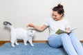 Girl reading book at cozy home. Girl smiling and petting furry cat Royalty Free Stock Photo