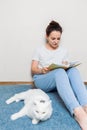 Girl reading book at cozy home. Girl smiling and petting furry cat Royalty Free Stock Photo