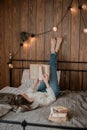 Girl reading a book and drinking coffee in bed feet on the wall. Royalty Free Stock Photo