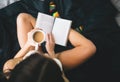 Girl reading book and drinking coffee on the bed. Top view of young woman read a book on black bed linen. Royalty Free Stock Photo