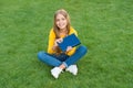 Girl reading book outdoors green lawn background, kids literature concept