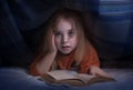 Child reading a book under the covers. Immersion into the magical world Royalty Free Stock Photo