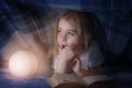 Child reading a book under the covers. Immersion into the magical world Royalty Free Stock Photo