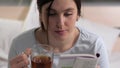 Girl is reading book. Young attractive caucasian woman sits in bed in evening and reads book and drinks black tea before Royalty Free Stock Photo