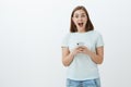 Girl received invitation to awesome party via messages in internet holding smartphone gazing amazed and delighted at