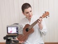 The girl is recording the lesson on a video camera. Broadcast the lesson. Online learning to play the guitar, ukulele. The girl