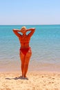 Girl in red bathing suit sunbathing standing on beach by sea. Beautiful woman Royalty Free Stock Photo