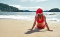 A girl in a red bikini and a santa hat is sunbathing on a sandy shore. Christmas in countries with a warm climate. Royalty Free Stock Photo