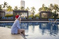 Girl in a red Christmas hat next to the swimming pool with blue water. Holiday concept. Royalty Free Stock Photo