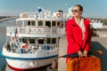 Girl in a red coat with a suitcase and an umbrella at the pier against the background of the ship Royalty Free Stock Photo